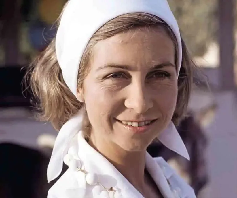 Retrato a color de la joven reina Sofía de España, sonriente, con una banda blanca en el cabello y una blusa blanca.