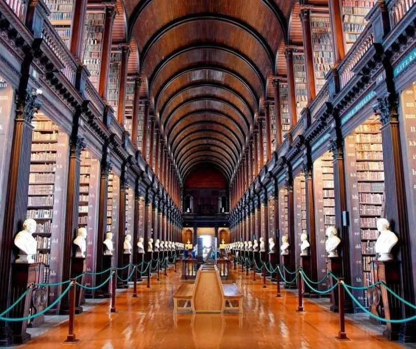 Interior de la biblioteca del Trinity College en Dublín, Irlanda, con techos abovedados, estanterías de madera y bustos 