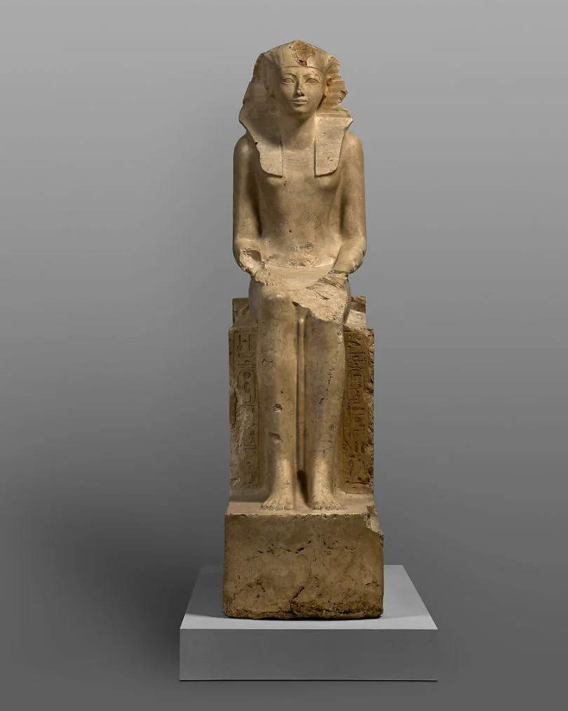 Hatshepsut aparece con el tocado nemes y la falda ceremonial shendyt, atributos tradicionales del faraón, pero la escultura conserva rasgos femeninos y títulos escritos en femenino. Foto- The Metropolitan Museum of Art · Public Domain.